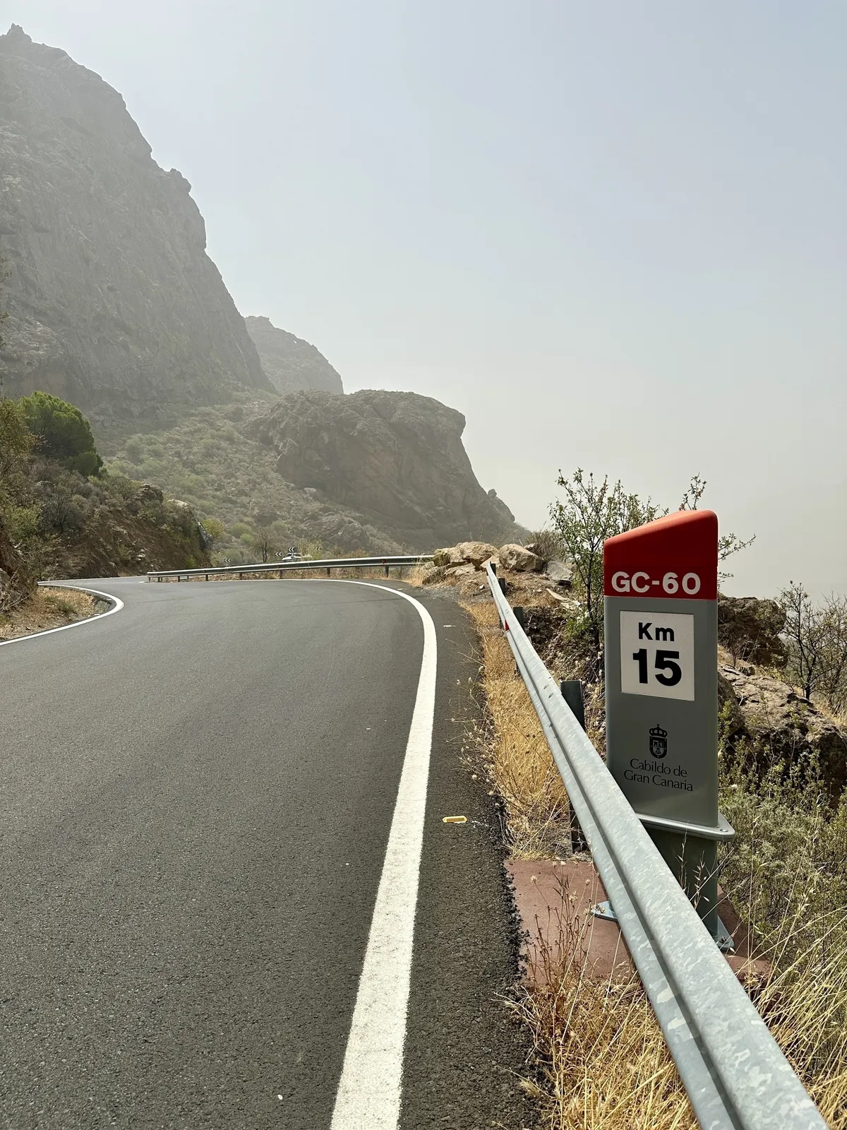 Eine kurvenreiche Bergstraße auf Gran Canaria führt an einem Kilometerstein vorbei, umgeben von karger Landschaft und Felsen.