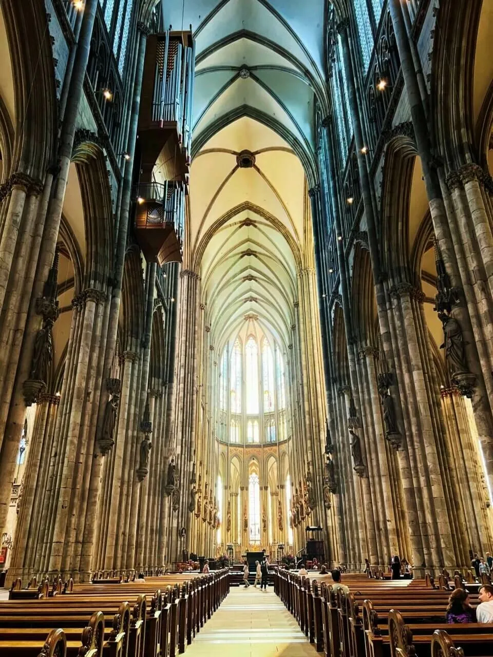 Blick in das beeindruckende, hohe Mittelschiff des Kölner Doms mit gotischen Säulen, Gewölbe und langen Kirchenbänken.