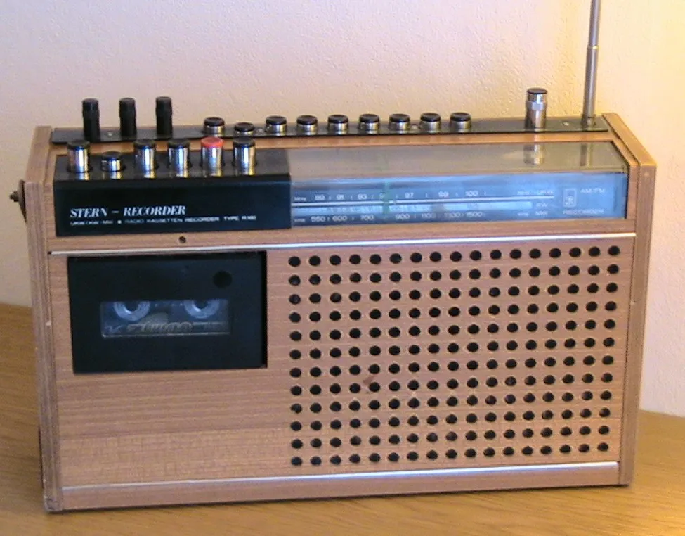 Der DDR Radio-Recorder Holzstern R160 aus Holz mit einer perforierten Front, einer Kassettenschublade auf der linken Seite und einem analogen Tuner-Bereich mit verschiedenen Reglern und Knöpfen an der Oberseite. Es gibt auch eine Antenne auf der rechten Seite.