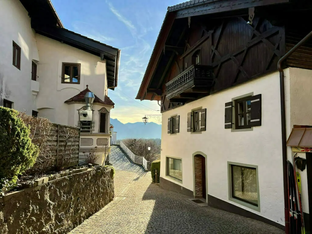 Enge, gepflasterte Gasse mit historischen Häusern und Bergblick im Hintergrund.
