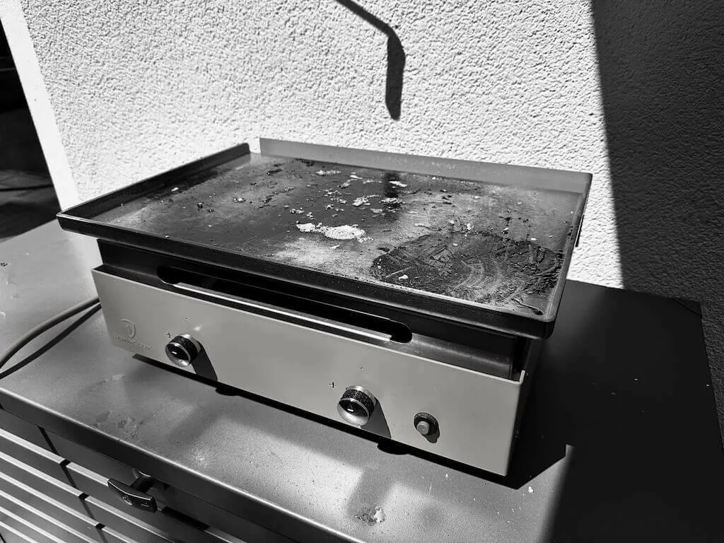 Eine Plancha mit zwei Reglern steht auf einer Metalloberfläche.