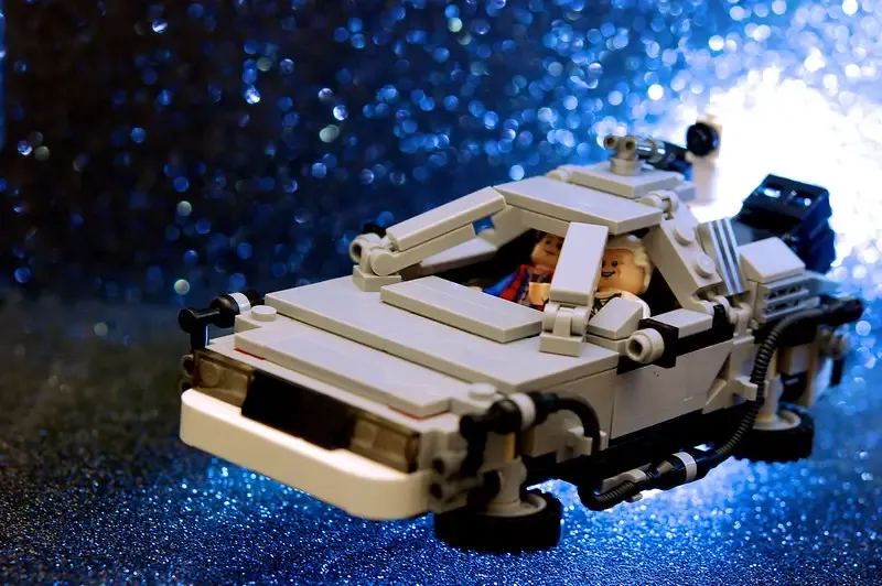 Ein detailgetreues Modell eines LEGO-Autos, das einer bekannten Zeitmaschine aus einem Film ähnelt. Zwei Figuren sitzen im Inneren des Fahrzeugs vor einem glitzernden, blauen Hintergrund.