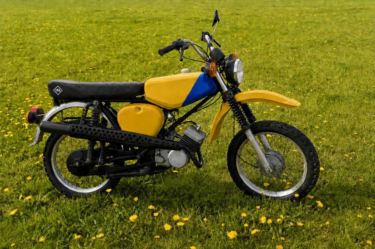 Gelbe Simson im Gelände-Look mit blauem Seitenteil, hochgelegtem Auspuff und schwarzer Sitzbank auf einer blühenden Wiese.